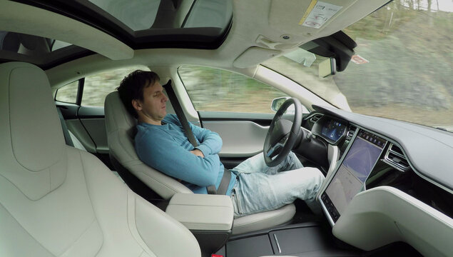 Male driver sleeping behind the wheel in self-driving autonomous electric car