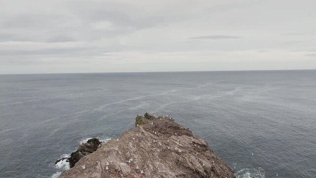 Backwards reveal drone shot of Bow Fiddle Rock, Portknockie, Moray coast, Scotland, overcast sky, dramatic sea arch emerging into frame