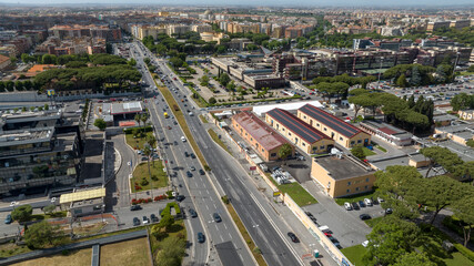 Fototapeta premium Panorama of Via Tuscolana near Cinecittà, in Rome, Italy. Aerial view of a major urban boulevard with multiple traffic lanes, surrounded by commercial buildings, residential districts, and green areas