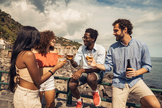 Multicultural friends toasting craft beer together by the sea in summer