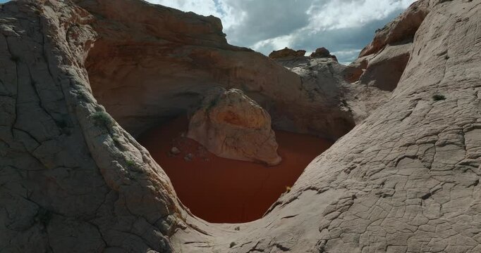 Smooth white sandstone basin encloses rust colored sand beneath dramatic desert sky, Cosmic Ashtray Utah