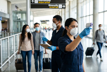 Obraz premium Airport biosecurity personnel measuring passenger temperature with infrared thermometer