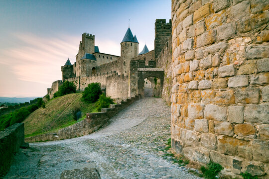Historic medieval fortress of Carcassonne with ancient stone walls, towers, and a cobbled path, inviting tourism and exploration of this iconic French destination under a soft sky.