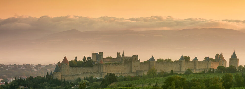 Historic fortified city stands majestically at sunrise over vineyards and a misty landscape, a prime travel destination in Carcassonne, France.