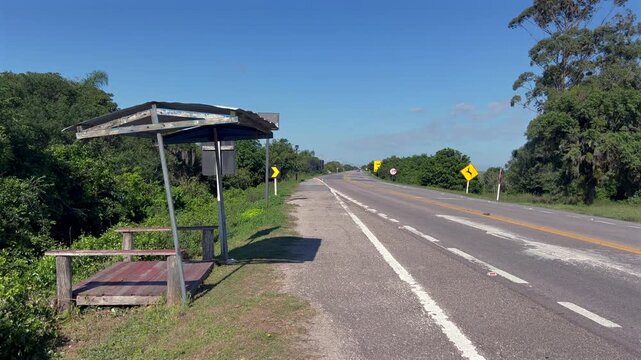 Static shot of a bus stop shelter on the rural entrance road at Taim Ecological Reserve, with trees, grass, and road signs