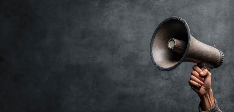 Hand holding gray metal megaphone with conical shape and smooth surface for loud announcements