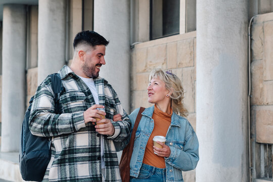 Happy couple enjoying coffee together outdoors, walking arm in arm, laughing, and sharing a moment in the city