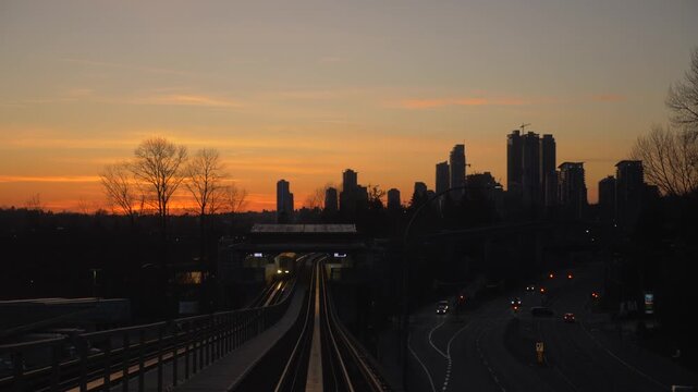 Skytrain approaching station at sunset with city skyline and highway traffic in Vancouver Canada.