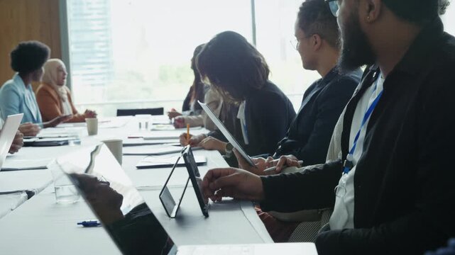 Professionals attending a conference or seminar, actively engaged in a meeting. People are focused, using laptops and tablets for notes and presentations in a collaborative and learning environment.