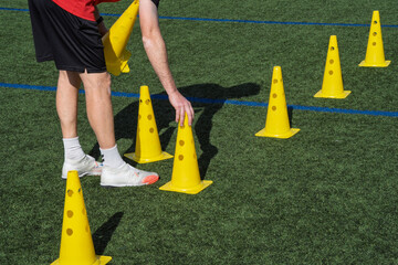 Coach preparing a soccer field for training drill, arranging yellow cones on green turf sports ground © Alejandro
