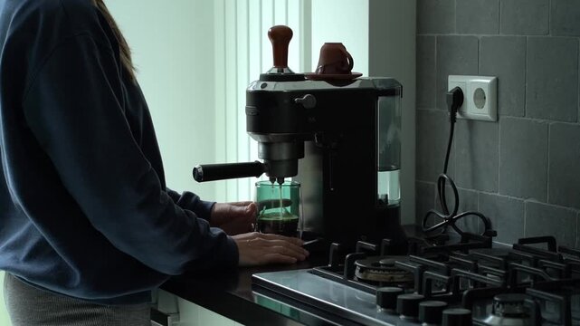 A woman prepares morning coffee using a stovetop moka pot, grinding beans and brewing fresh espresso in her home kitchen for a daily caffeine ritual. Lifestyle blogs, coffee culture articles