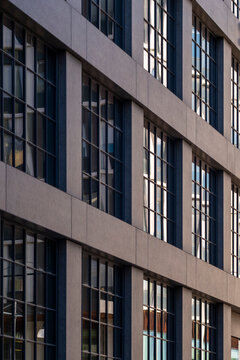 Concrete facade with tall windows set in a precise grid on an office building where urban shadow and exterior architecture emphasize vertical detail