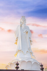 Fototapeta premium white lady buddha statue under colorful sunset sky