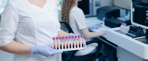Medical laboratory technician presenting rack of blood sample tubes for clinical diagnostics and testing with analyzer in lab © Parilov