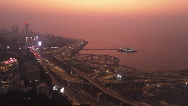 Aerial view of the Coastal Road interchange and Haji Ali Dargah during a hazy sunset with the city skyline in the background Mumbai, Maharashtra, India.