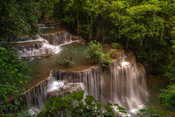 A turquoise waterfall cascades down in layers in the middle of the forest. © Pongsorn
