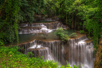 A turquoise waterfall cascades down in layers in the middle of the forest. © Pongsorn
