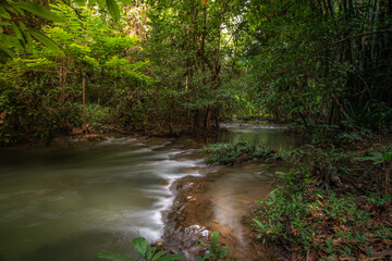 A turquoise waterfall cascades down in layers in the middle of the forest. © Pongsorn