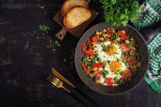 Rustic Skillet Eggs with Tomatoes and Herbs on Dark Background. Top view