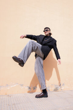A young man with one leg raised in a dynamic pose in front of a peach-colored outdoor wall