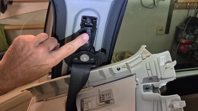 Car interior repair hand removing pillar trim panel exposing seatbelt mechanism automotive maintenance DIY project