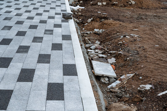 Designated paving boundary. Paved zone meets debris and dirt. Decorative stepping stones adjacent to rubble and dirt. Mosaic pavement concludes with debris and uncleaned urban site features