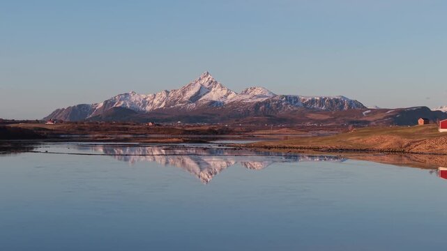 Snow capped mountains reflect in still water by the river in the early morning