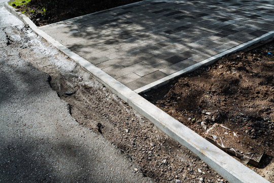 Updated sidewalk borders with gravel base. Transition zone between fresh concrete and natural earth surface. Edge details of pavement where it meets soil with trench and gravel base