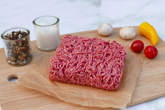 Frisches Rinderhackfleisch auf Holzbrett mit Gew&uuml;rzen. 