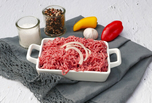 Frisches Rinderhackfleisch in einer wei&szlig;en Auflaufform, mit Zwiebelringen und Gew&uuml;rzen.