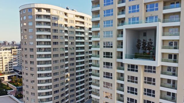 Two large apartment buildings are visible, with multiple floors and large windows. They are located in an urban area with a clear sky and bright sunlight.