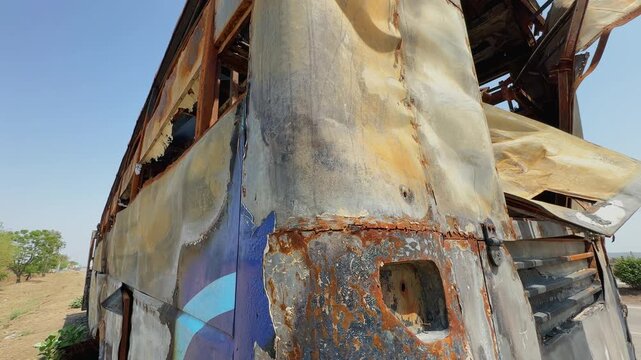 Orbiting shot around the rear section of a fire damaged sleeper bus showing rusted metal body, scorched panels and severe burn destruction outdoors