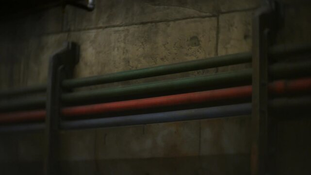 Pipes aligned in rows along a concrete corridor wall, secured by metal supports and stretching into the background. Dim ceiling lights illuminating the scene while perspective emphasizes industrial de