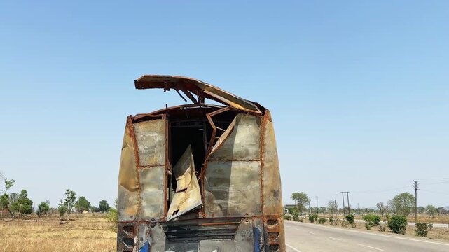 Rear view of a fire destroyed sleeper bus parked beside a highway with twisted metal panels, open damaged body and severe burn aftermath!