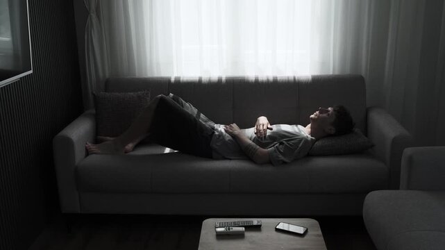 Young man lying on sofa and staring at ceiling in silence, depression, emotional emptiness, apathy, loneliness and loss of purpose in modern life concept