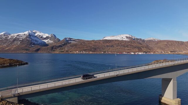 Driving across a bridge over water with mountains in the background on a sunny day