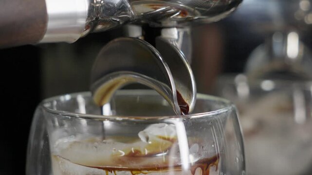 Close-up of espresso flowing from machine spout into glass with ice in caf&eacute; setting