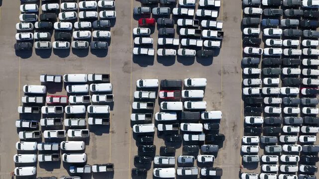 Numerous brand new commercial vans parked in orderly rows at a factory distribution center, waiting for sale or shipment, representing the automotive industry and mass production concepts