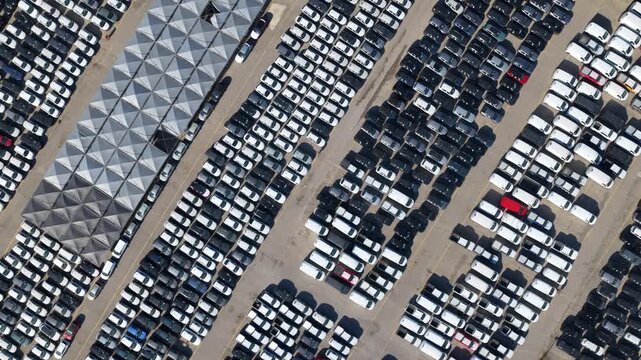 Top down aerial view of thousands of new cars parked in neat rows at an automotive plant, ready for shipping &mdash; mass production, logistics and distribution in industry