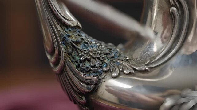 Closeup of ornate antique silver teapot handle with intricate floral engraving.