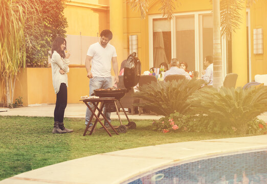 Middle Eastern family enjoying backyard barbecue and poolside gathering with friends at modern home