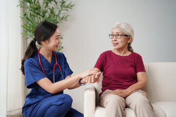 Obraz premium Young Asian nurse discussing health with an elderly woman at home, holding her hand while providing support and conveying empathy during the healthcare visit