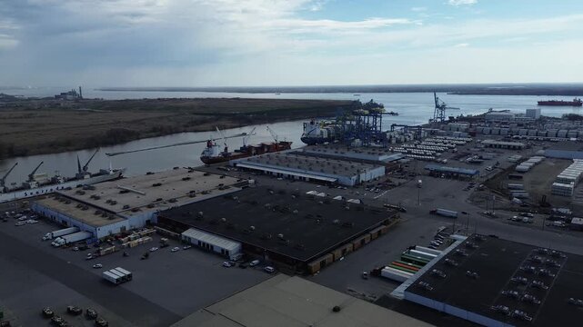 Christina river terminals stretch along Christina River beside River Road with ships berthed at active loading piers. Warehouse roofs, container grids, crisp sunlit surfaces create patterns, DE