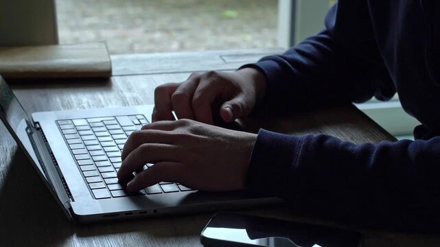 A programmer works on a computer near a window, creating a productive home workspace that saves commuting time and improves work-life balance. Remote work articles, software developer lifestyle blogs