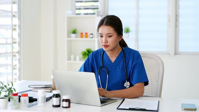 Doctor working in medical office using laptop computer and writing or taking note in notebook.