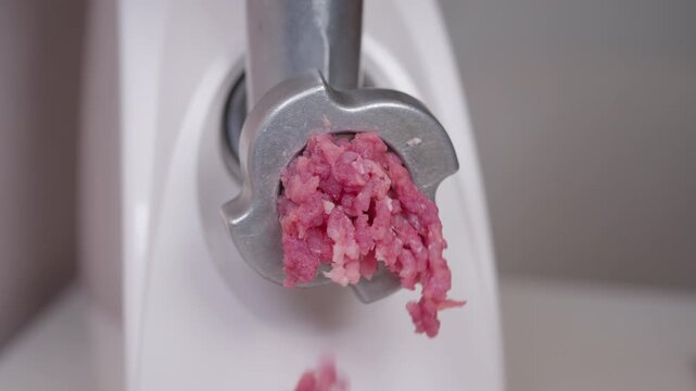 Meat grinding closeup. Robust stainless steel machine extrudes vibrant pink meat strands. Detailed view of raw pork being processed by electric meat grinder in kitchen setting