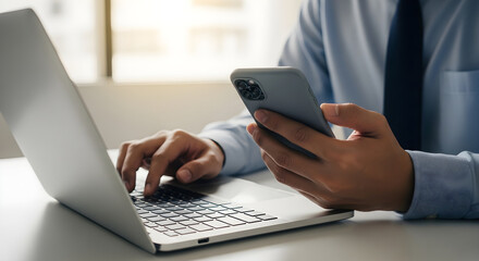 Fototapeta premium Man in office working on laptop and holding smartphone device