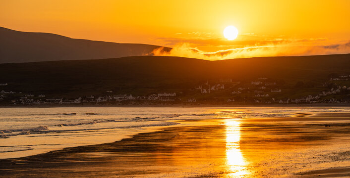 Golden sunset over Keem Beach on Achill Island, County Mayo, Ireland. Atlantic waves and wet sand reflect the evening sun beneath the hills of the Wild Atlantic Way.
