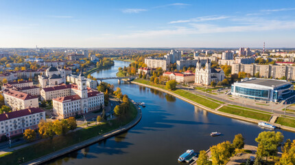 Obraz premium Aerial view of a European city with a wide river flowing through it, featuring modern and historic architecture under a clear blue sky.