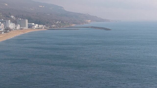  Calm ocean landscape with a narrow breakwater reaching into blue water beneath a hazy horizon
